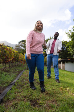 African American couple walking along grassy vineyard path, woman wearing pink sweater smiling