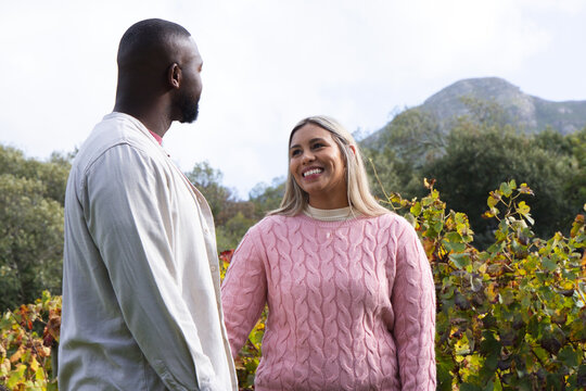 African American couple standing among grapevines, woman in pink sweater with pendant, man looking