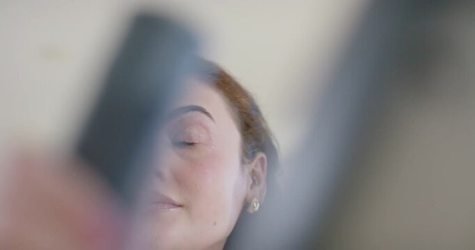Adult woman opening eyes, tilting upward in room while front hand lifting tools for makeup