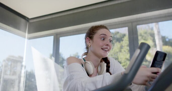 20s woman leaning forward, reacting to incoming call, tapping phone on home bike with headphones