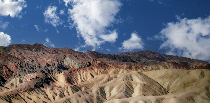 View of the colorful, eroded badlands of Zabriskie Point with dramatic ridges and deep shadows under a bright blue sky in Death Valley, California, United States.
