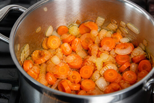 Chopped vegetables and shrimp are simmering in a stainless steel pot on a stovetop.