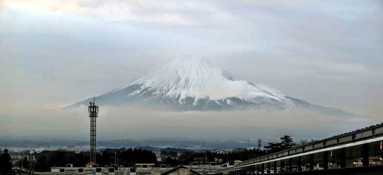 View of Mount Fuji with snow-capped peak rising above low-hanging clouds and urban rooftops in Fujinomiya, Shizuoka, Japan.