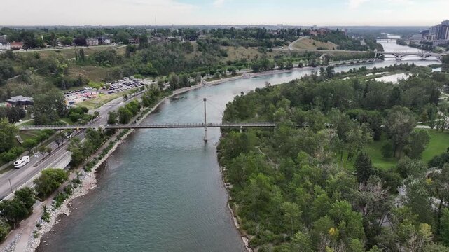 flying above Bow River next to Prince&rsquo;s Island Park towards Centre St Bridge, while crossing Bow River Pathway Bridge with parts of Skyline of Downtown Calgary ( Alberta, Canada) on right side, video