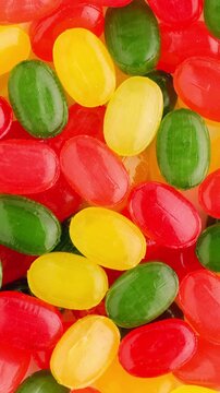 Colorful Hard Candies Rotating Smoothly in Macro. Oval red, yellow and green candies turn slowly, forming a bright glossy confectionery background.