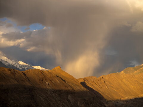 View of Hopper Glacier View point with rugged mountain slopes illuminated by golden hour light under dramatic storm clouds in Hunza Nagar, Gilgit Baltistan, Pakistan.