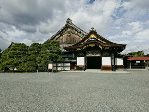 View of Nijo Castle featuring traditional Japanese architecture with ornate wooden gates and manicured pine trees under a cloudy sky in Kyoto, Kyoto, Japan.