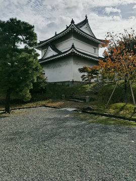 View of the traditional white turret of Nijo Castle with its dark tiled roof, stone foundation, and surrounding trees under a cloudy sky in Kyoto, Kyoto, Japan.