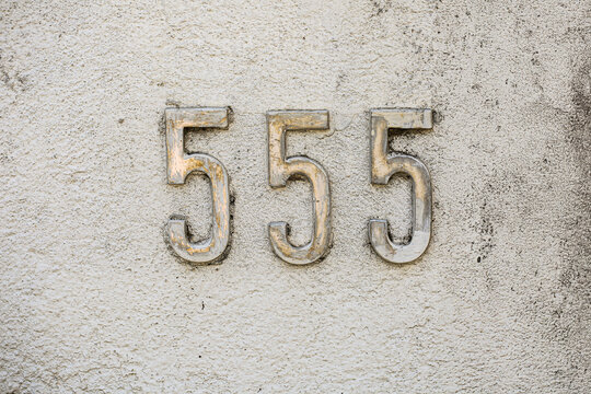 555 house number sign on weathered stucco wall, vintage metal digits with worn silver paint, rustic textured plaster background, aged building address plate