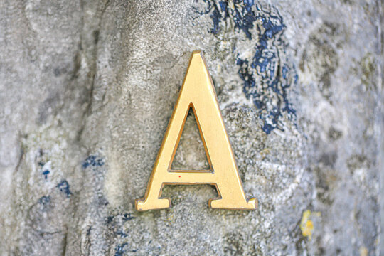Letter A in polished brass mounted on rough stone wall, elegant metallic signage design representing address or monogram initial symbol closeup