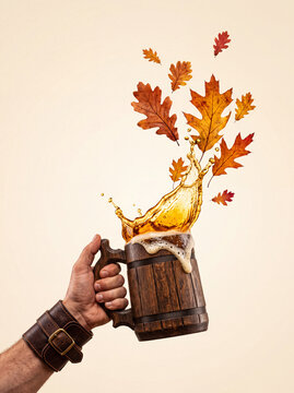 Hand holding wooden beer mug with splashing beer and autumn leaves