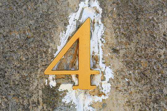 Number 4 in metal displayed on rough textured wall with plaster patches, vintage house address sign showing weathered aged rustic surface details