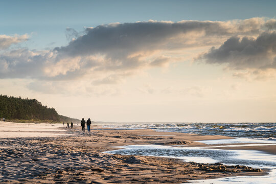 View of people walking along the sandy beach at the Baltic Sea coast under a cloudy sky in Sztutowo, Pomeranian Voivodeship, Poland.