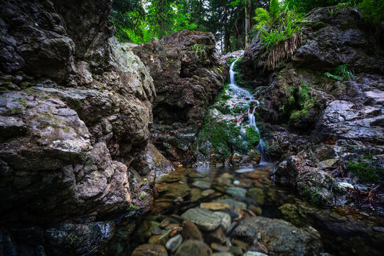 View of a small waterfall cascading over moss-covered rocks in a lush forest setting with clear water flowing into a rocky pool in Karpacz, Lower Silesian Voivod, Poland.