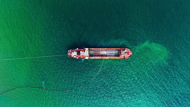 Aerial view of ship towing containment boom, Black Sea, Bulgaria. Red hulled vessel pulls a floating cable across deep green water, seen directly overhead.