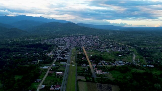 Wide Aerial View of Tropical Ecuador Town and Highway in Mountain Valley, Green Forest, Rural Development and Dramatic Cloudy Sky