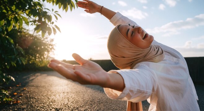 Joyful young woman with hijab embracing the golden hour sunlight outdoors