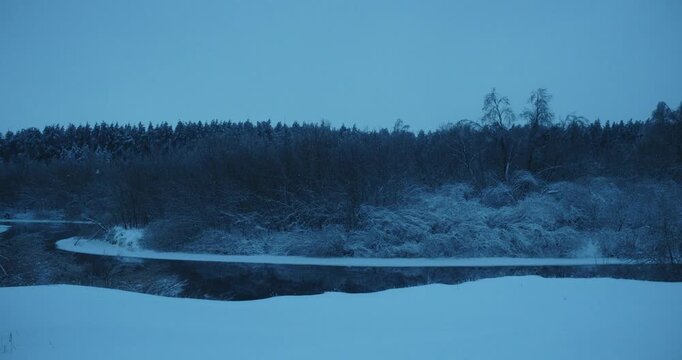 Ice Floes Drifting on Spring River Against Snowy Forest at Dusk
