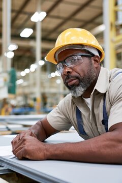Industrial factory worker with yellow helmet and safety goggles in workshop for workplace safety training and manufacturing industry poster design