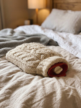 Hot Water Bottle with Knitted Wool Cover Lying on Cozy Bed