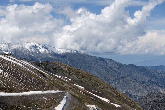 View of the winding road leading to Babusar Top, surrounded by snow-capped mountain peaks and dramatic clouds in Naran, Khyber Pakhtunkhwa, Pakistan.