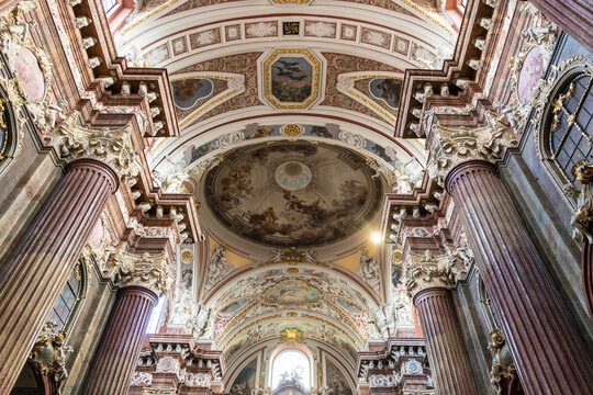 View of the ornate interior of the Poznan Fara Basilica, featuring grand columns, intricate baroque ceiling frescoes, and gilded architectural details in Poznan, Greater Poland, Poland.