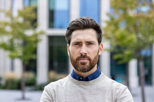Close-up portrait of a young male businessman standing outside and looking confidently and seriously at the camera
