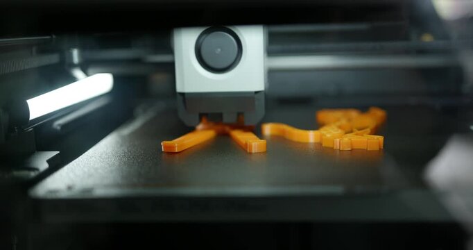 3D printer creates orange keychains at workshop in afternoon