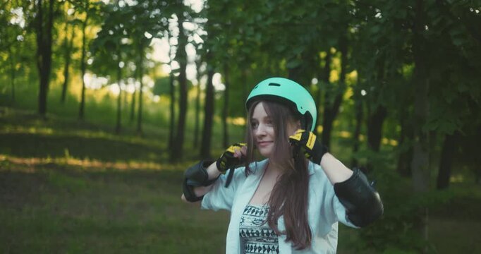 Young woman prepares to skate in a park with green trees on a sunny day in late afternoon