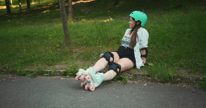 Girl sitting on grass while putting on roller skates in a park during daytime
