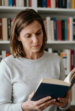 Lifelong learning and personal growth mature woman reading a book in a home library for education self improvement and quiet leisure time activity