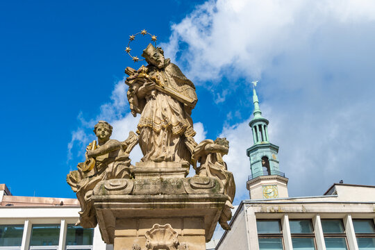 View of the stone statue of Saint John of Nepomuk with a star halo and sculpted angels, set against a blue sky and a historic church tower in Poznan, Greater Poland Voivod, Poland.