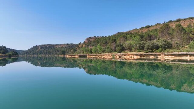 Flight low over the oasis of mirrored waters of Ruidera Lagoons in Spain's Castilla La Mancha region. Clean green blue waters mirror the sculpted banks, lush green hills, and perfect blue skies.