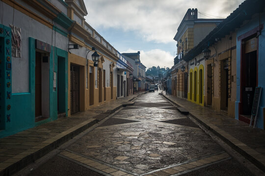 View of a historic cobblestone street lined with colorful colonial buildings under a cloudy sky in San Cristobal de las Casas, Chiapas, Mexico.