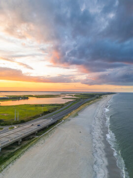 View of the coastal highway running alongside the sandy beach and marshlands during a vibrant sunset in Bethany Beach, Delaware, United States.