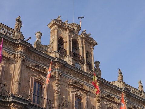 View of the ornate facade and clock tower of the historic town hall in Plaza Mayor, featuring intricate stone carvings, statues, and Spanish flags in Salamanca, Castile and Leon, Spain.