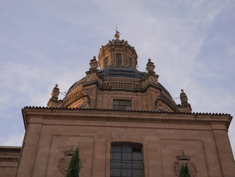 View of the ornate stone dome of the Clerecia church featuring detailed architectural carvings and a weather vane against a soft evening sky in Salamanca, Castile and Leon, Spain.