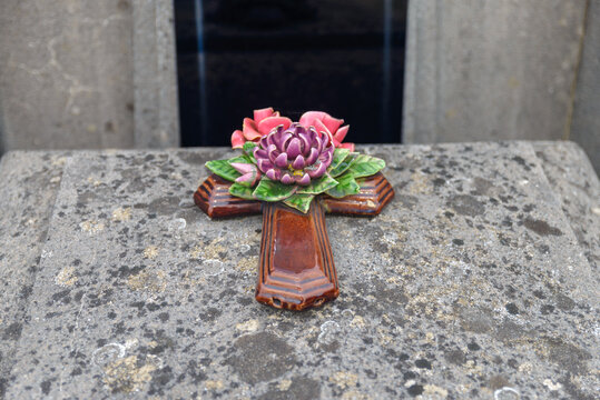 Croix fun&eacute;raire en fa&iuml;ence &eacute;maill&eacute;e avec fleurs en relief sur une tombe