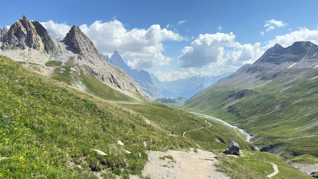 Mountain valley alpine landscape steep slopes green forests harvested hayfield wooden hut cloudy sky distant ridges nature scenery wilderness view
