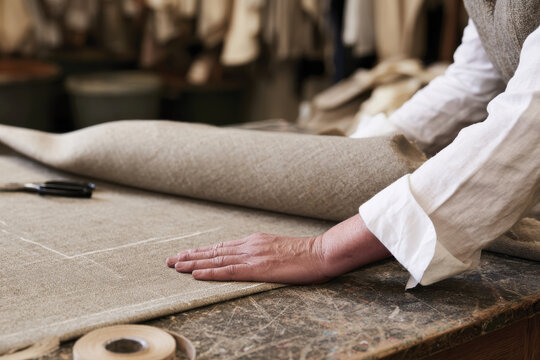 A skilled artisan carefully lays out fabric on a table, showcasing craftsmanship and dedication in the textile creation process within a cozy, creative workshop environment.