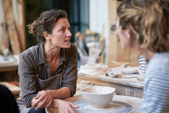 In a dynamic pottery studio, a ceramic artist engages in a lively discussion with students, fostering creativity and sharing valuable insights into pottery techniques and artistic expression.
