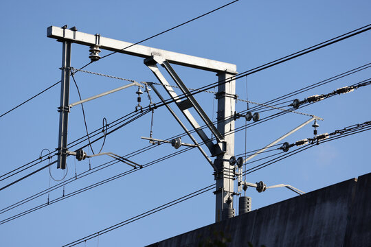 View of overhead railway electrification infrastructure with catenary wires and a steel support mast against a clear blue sky in Rouse Hill, New South Wales, Australia.