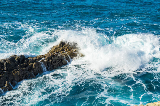 View of the rugged volcanic cliffs being hit by powerful turquoise ocean waves, creating white sea spray along the coastline in Ajuy, Fuerteventura, Spain.