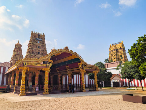 View of the ornate golden gopuram and traditional architecture of Nallur Kandaswamy Kovil in a sandy courtyard under a clear blue sky in Jaffna, Northern Province, Sri Lanka.