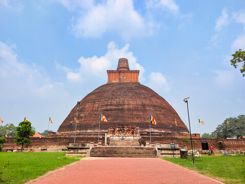View of the historic Jetavanaramaya stupa with its massive brick dome and square base, surrounded by green lawns and Buddhist flags in Anuradhapura, North Central Province, Sri Lanka.