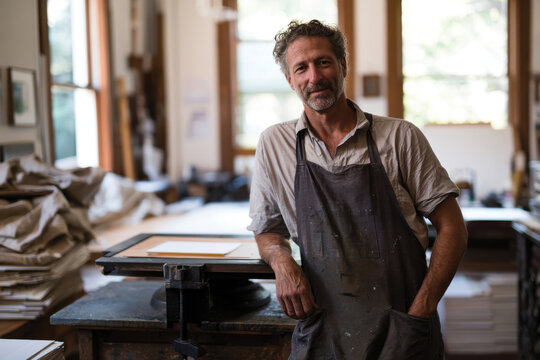 A skilled artisan stands confidently in a bright workshop surrounded by printmaking tools, showcasing creativity and passion in the artistic process of printmaking.