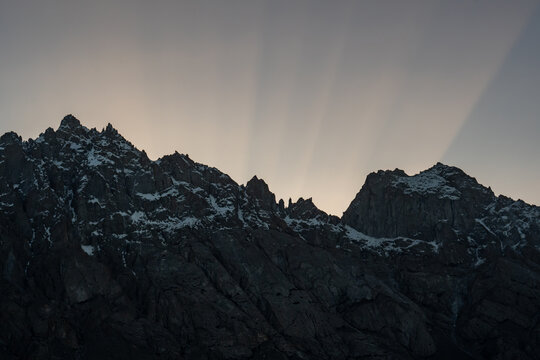 View of the Haldi Cones with snow-capped peaks and dramatic crepuscular rays shining over the mountain ridges in Machlu, Gilgit, Pakistan.