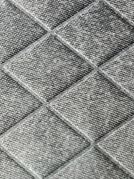 Fondo de textura geom&eacute;trica con patr&oacute;n de rombos en relieve sobre material textil gris oscuro, ideal para conceptos de dise&ntilde;o industrial, tecnolog&iacute;a y automoci&oacute;n