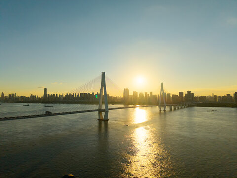 The sun sets over the modern city skyline and the large cable stayed bridge crossing the river in Wuhan China
