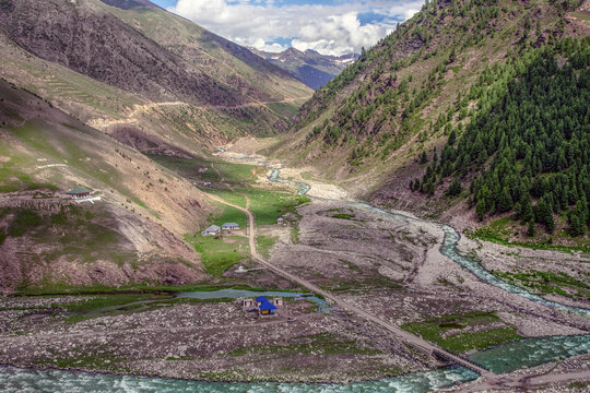 View of the river flowing through the valley surrounded by rocky terrain, green slopes, and mountain peaks in Batakundi, Khyber Pakhtunkhwa, Pakistan.